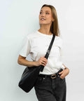 Kvinde der har en sort VEGA taske på, fra IGEN, og bær den crossbody med sølv swirl-hardware.
