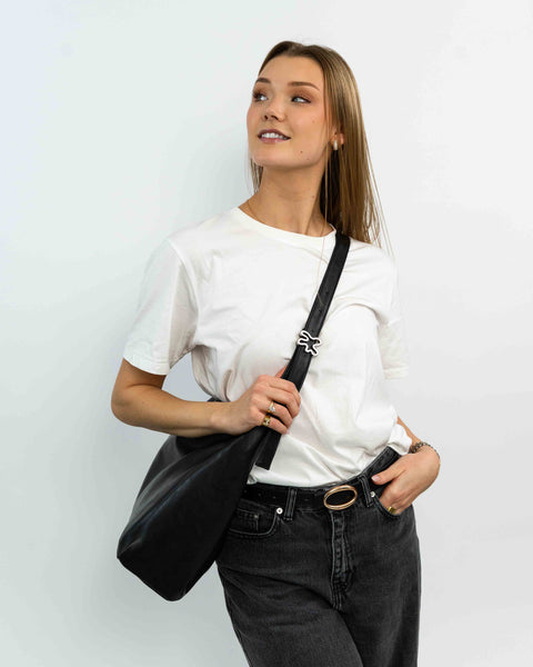 Kvinde der har en sort VEGA taske på, fra IGEN, og bær den crossbody med sølv swirl-hardware.